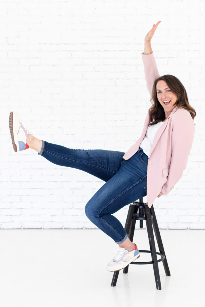Woman sitting on stool, smiling with leg and arm in the air