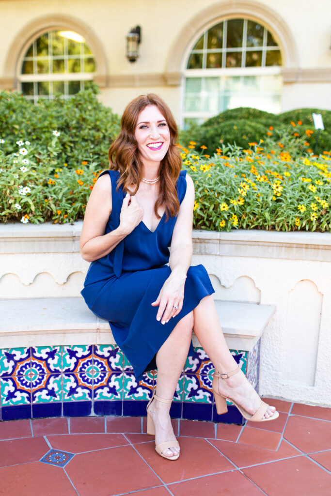 Woman in blue dress sitting on a bench and smiling with legs crossed