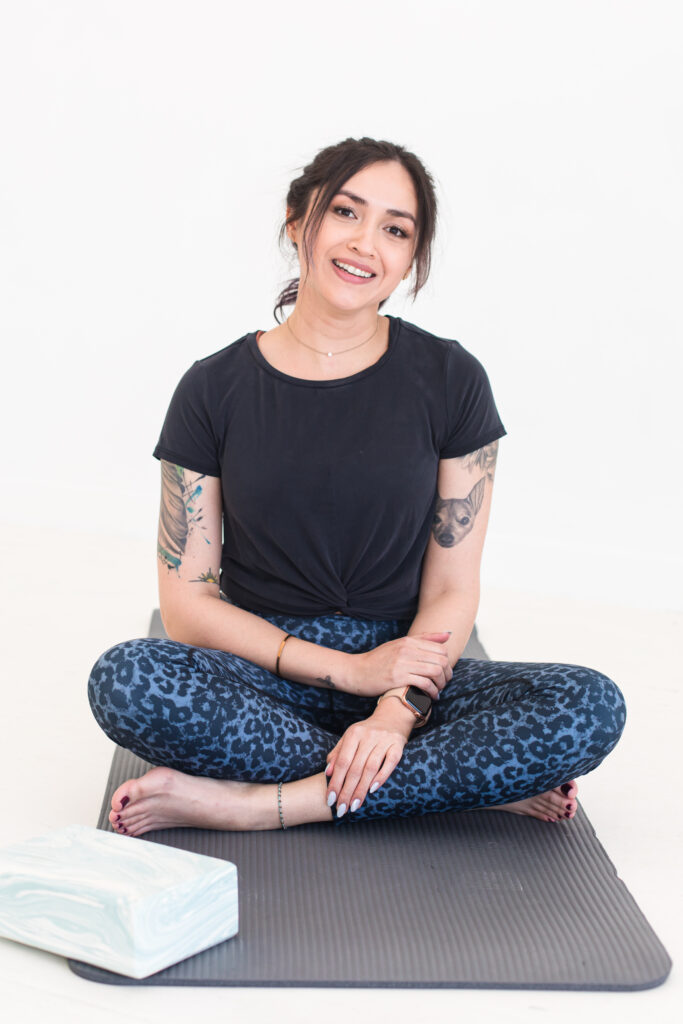 Woman in yoga gear sitting cross legged on a yoga block with 